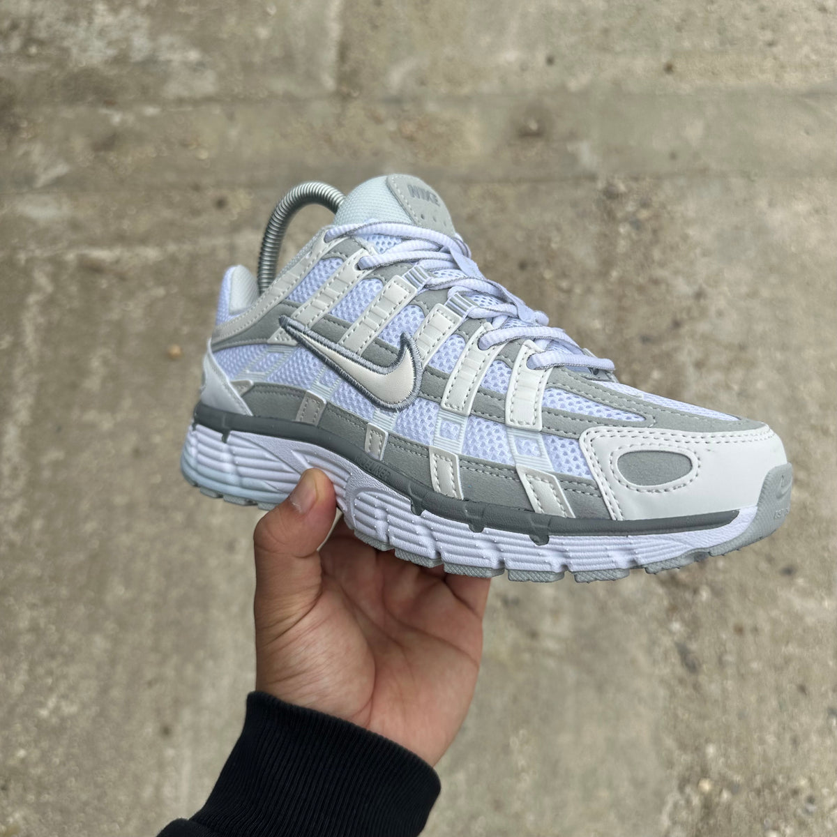 A light grey and white Nike sneaker held up by a hand against a background of green grass.